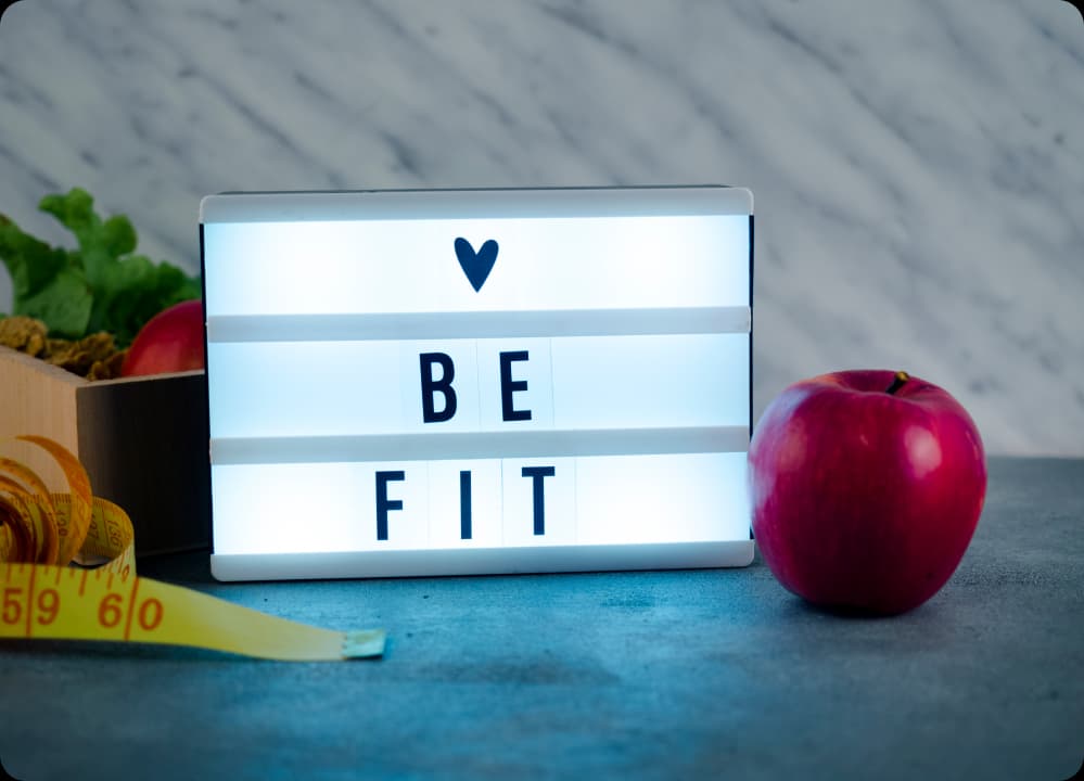 "Be Fit" sign with apple and measuring tape symbolizing healthy lifestyle and wellness choices for employees.