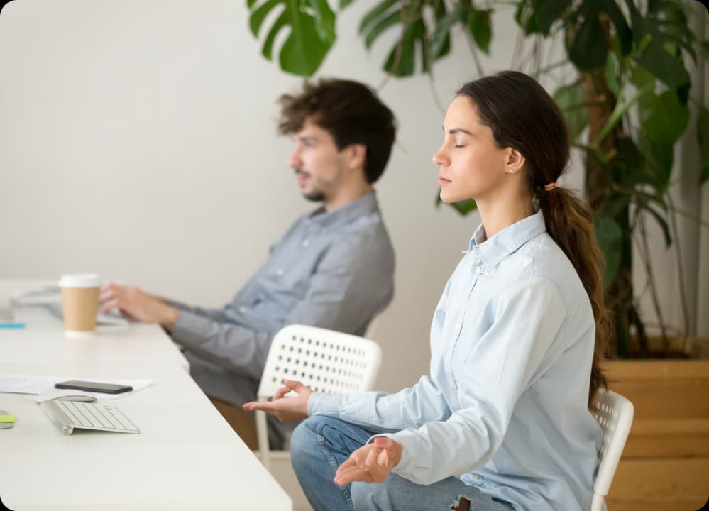 Woman meditating at desk in office, promoting brain health and stress reduction for workplace productivity.