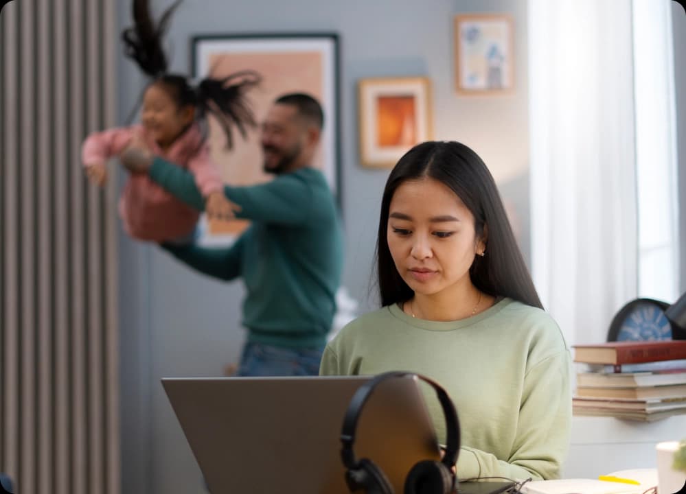 Woman working remotely while family plays in the background at home