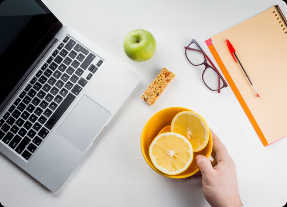 Healthy desk setup with fruits, granola bar, and laptop, highlighting functional nutrition choices at work for energy and wellness.