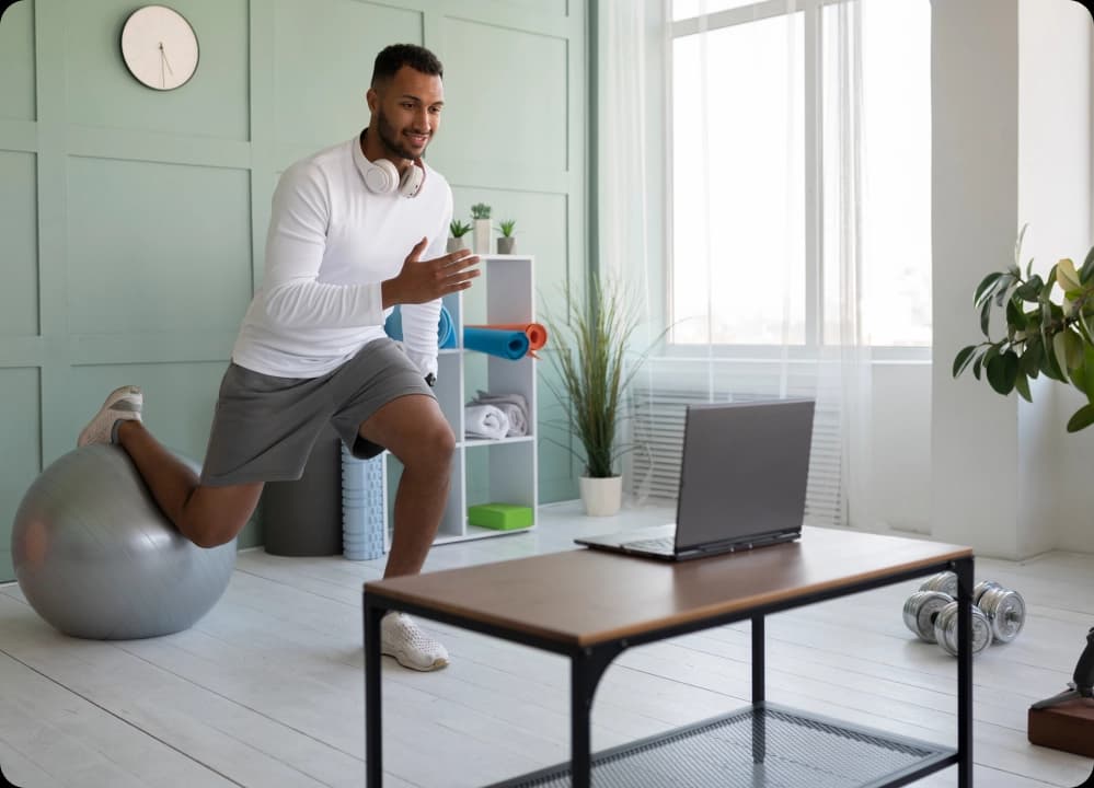 Man doing virtual workout on exercise ball during online fitness session at home