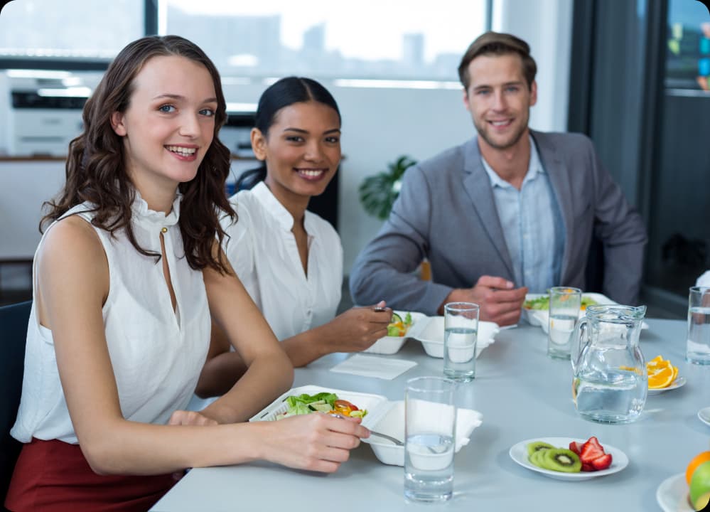 Smiling coworkers enjoying a healthy meal together in the office cafeteria, highlighting the benefits of corporate nutrition programs for employee health and team success.