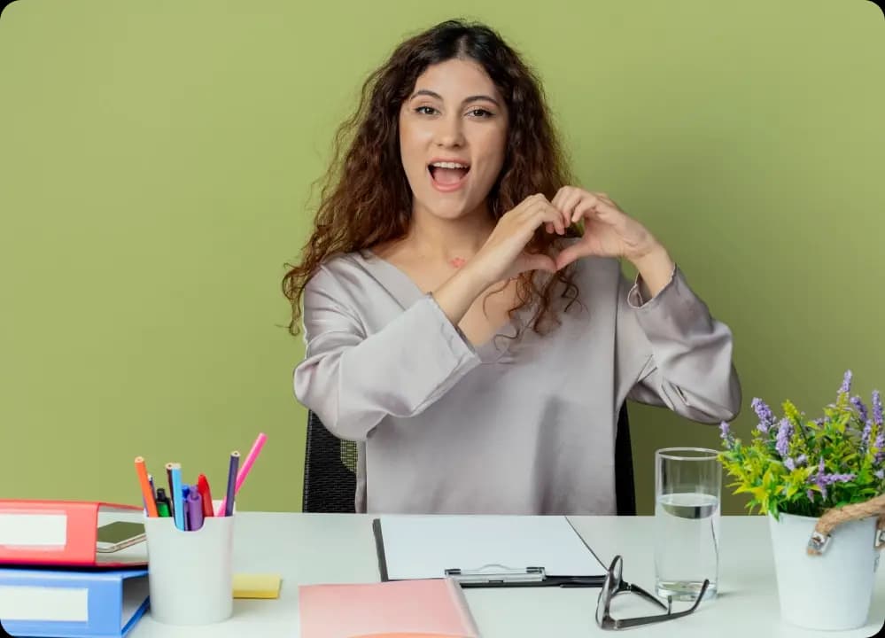 Smiling employee making a heart gesture with hands to promote positivity and workplace wellbeing