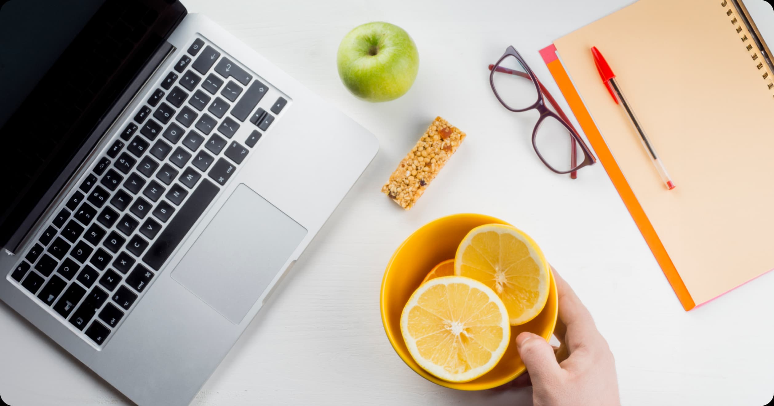 Healthy desk setup with fruits, granola bar, and laptop, highlighting functional nutrition choices at work for energy and wellness.