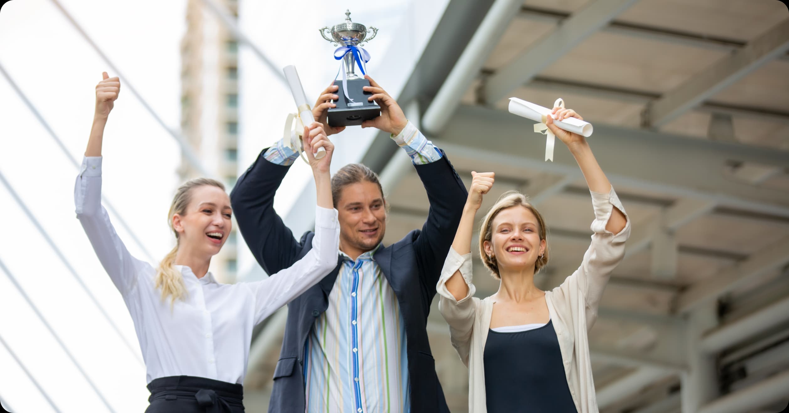 Happy employees celebrating with trophy and certificates, symbolizing the power of rewards and recognition in boosting wellness.