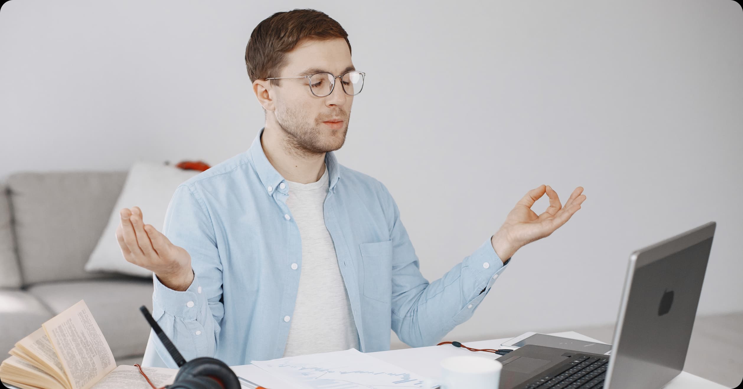 Man practicing mindfulness meditation at his desk while working on a laptop, promoting cognitive resilience in a high-pressure work setting.