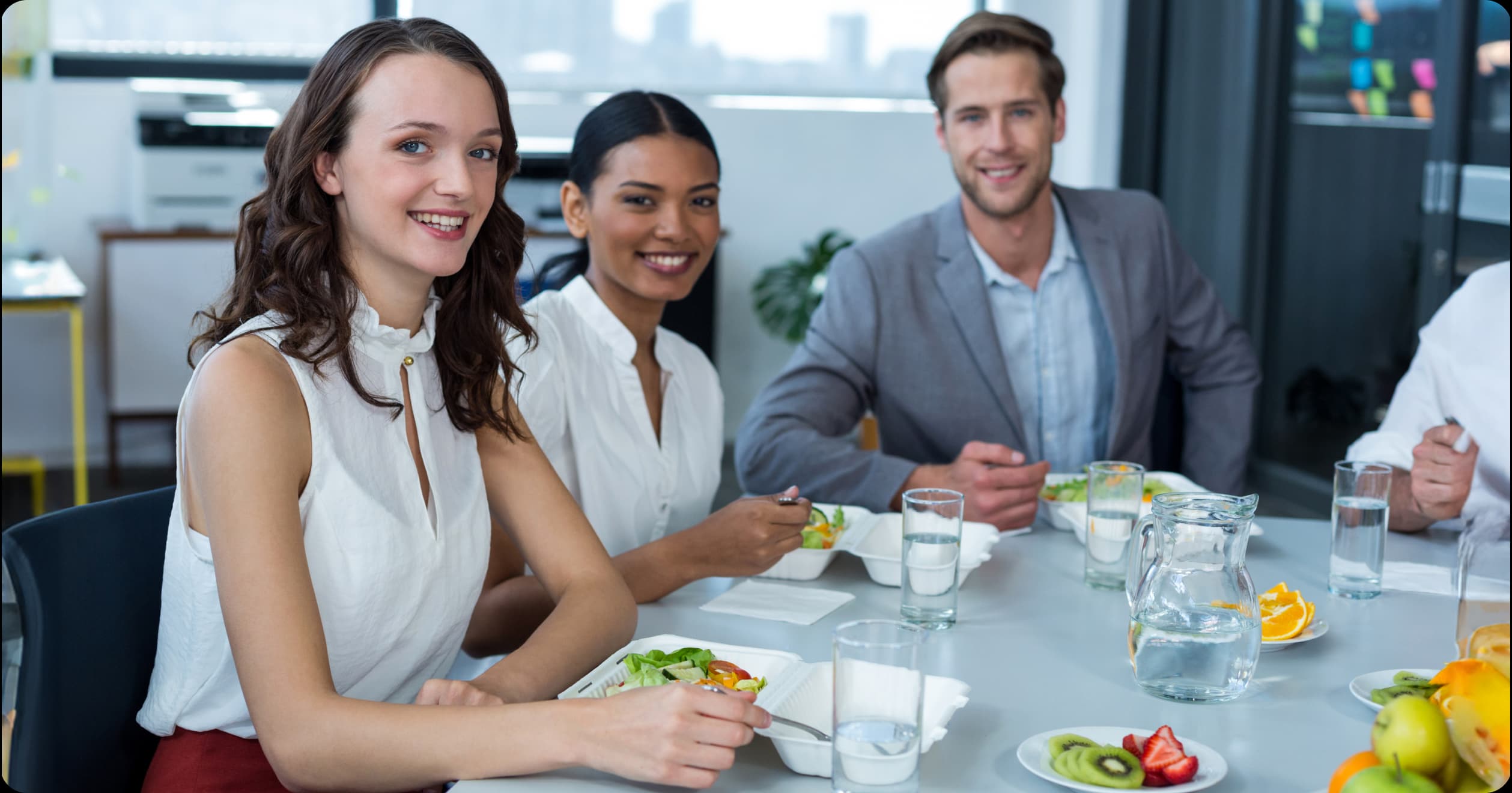 Smiling coworkers enjoying a healthy meal together in the office cafeteria, highlighting the benefits of corporate nutrition programs for employee health and team success.