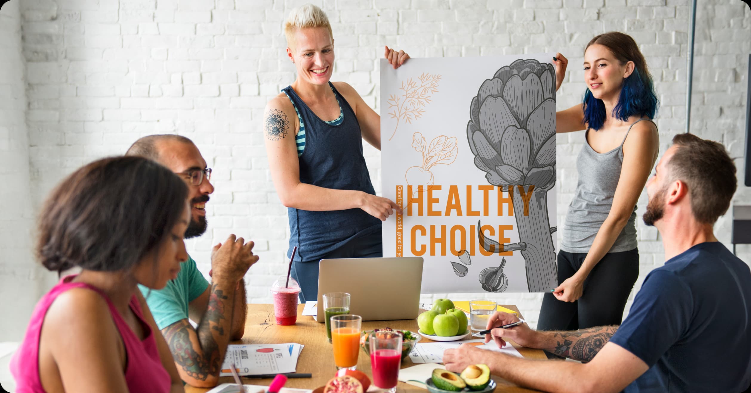 Team discussing healthy lifestyle choices with fresh food and a "Healthy Choice" poster, representing holistic health as a preventative strategy.